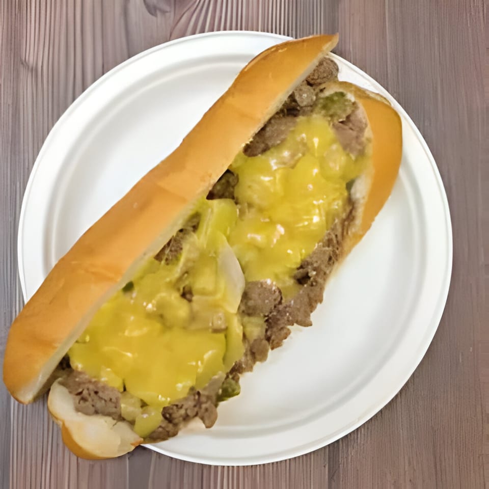 A NY Style Delicatessen cheesesteak sandwich with melted cheese and onions on a white plate.