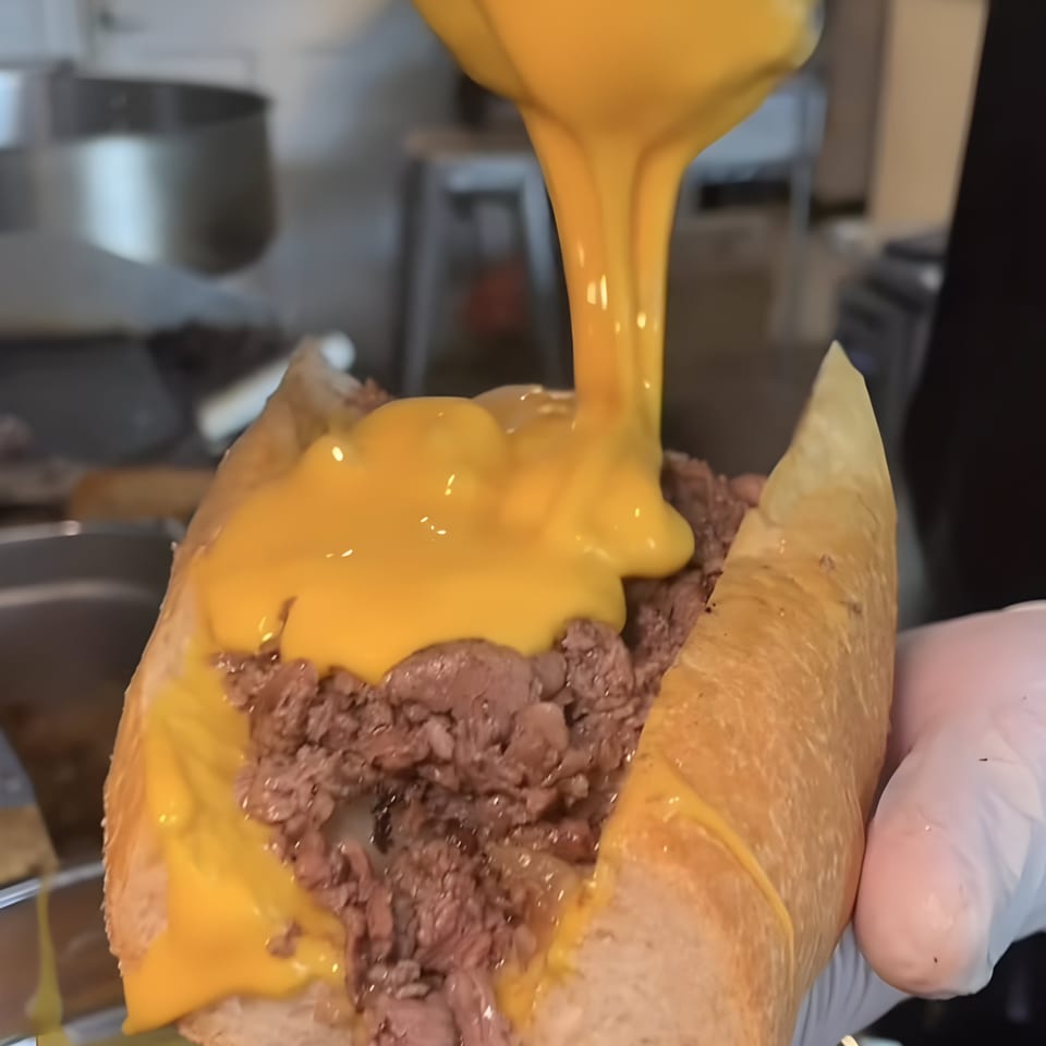 Cheesesteak sandwich from NY Style Delicatessen, with melted cheese sauce being poured over the meat.