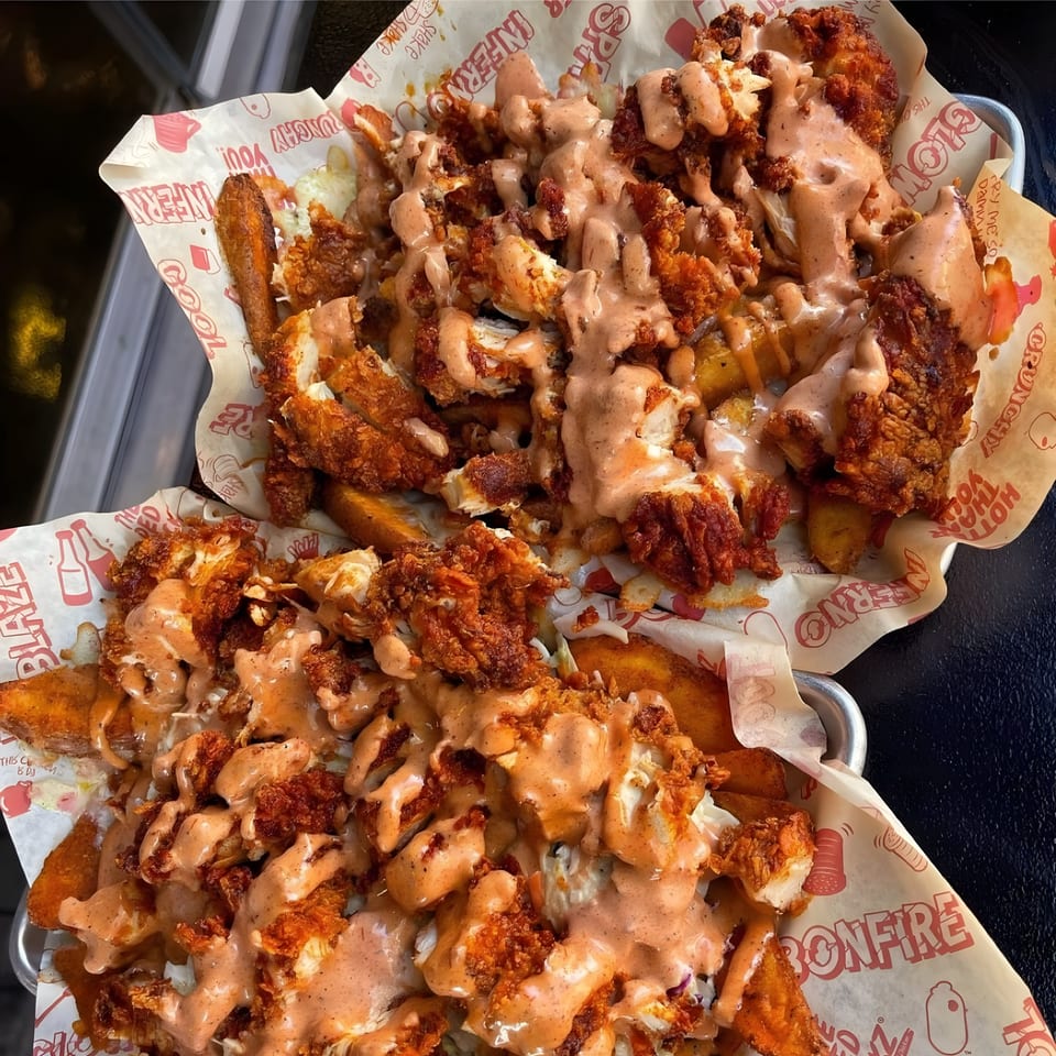 Two servings of crispy fried chicken and potato wedges, drizzled with creamy sauce in branded paper-lined baskets.