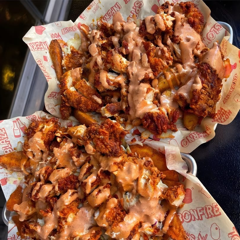 Two servings of crispy fried chicken and potato wedges, drizzled with creamy sauce in branded paper-lined baskets.