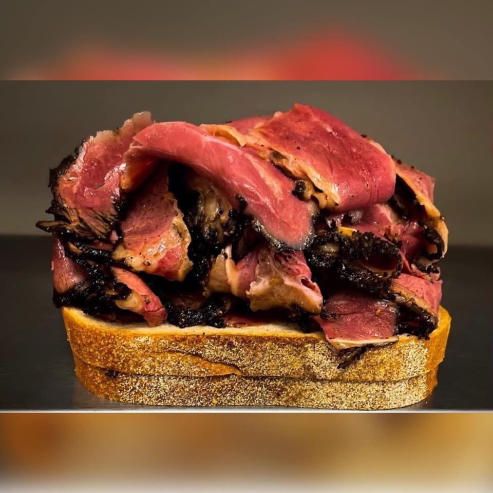 A towering NY Style Delicatessen pastrami sandwich on rye bread, piled high with juicy meat.